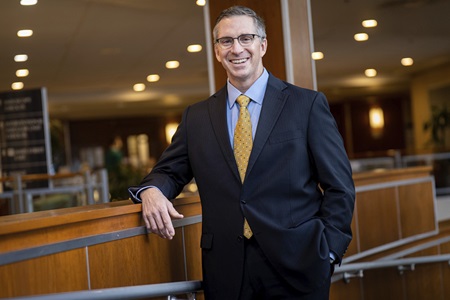 John Herman, CEO of Lancaster General Health, smiles and stands with one elbow resting on a wall.